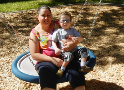 Mom holding young boy with glasses on swing
