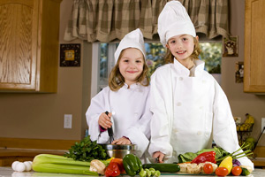 2 girls drwwed up as chefs in the kitchen preparing vegetables